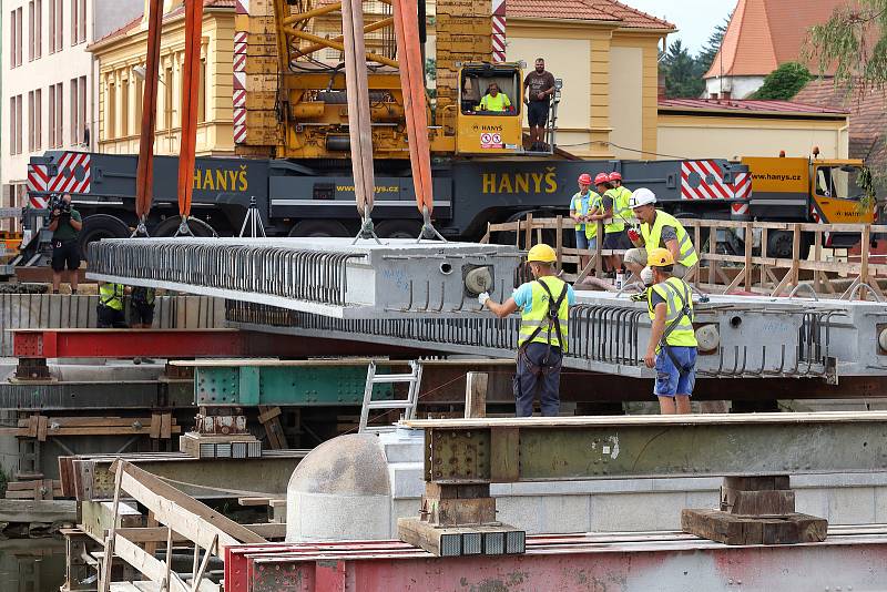 Největší kolový jeřáb v zemi v pondělí usadil na opravené pilíře deset betonových nosníků, z nichž se skládá nový most. Ten bude mít širší vozovku i vyšší nosnost. Řidiči se po něm projedou až příští rok.