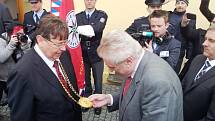 Prezident Miloš Zeman se vítá s hejtmanem Královéhradeckého kraje Lubomírem Francem a prohlíží si medaili na jeho krku.
