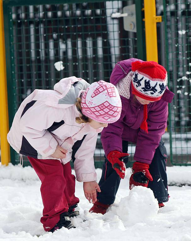 Děti z mateřské školy staví sněhuláka.