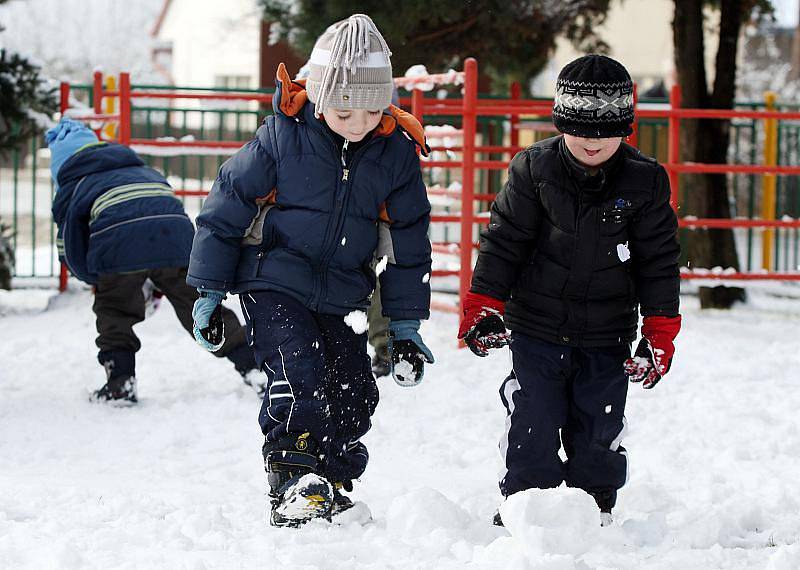 Děti z mateřské školy staví sněhuláka.
