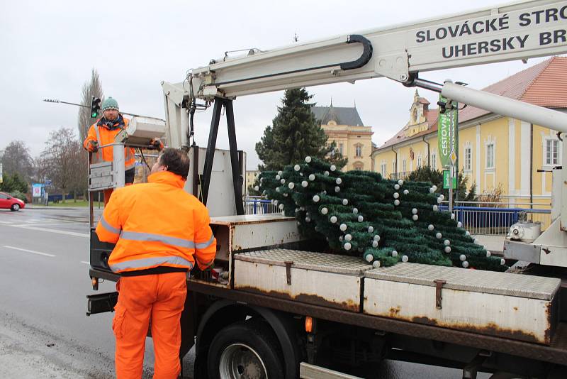 Zaměstnanci technických služeb uklízejí svítící sněhové vločky z ulic města. Další den je čekají ještě stromy.