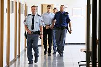 Eskorta vězeňské služby přivádí k soudu obžalovaného čtyřiadvacetiletého Lukáše Nováka. Měl zabít mačetou svého otčíma.
