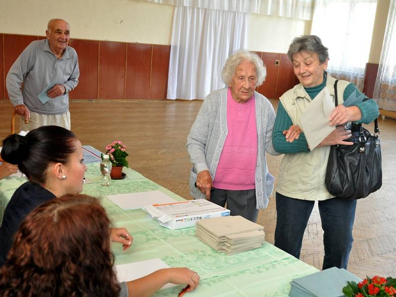 Nejstarší obyvatelka Zlínského kraje Vlastimila Češková (v růžovém), která letos na jaře oslavila 108 let, přišla v pátek 25. října 2013 do volební místnosti ve své obci jako první hned s úderem 14. hodiny. Doprovodila ji dcera Jana Kalhousová.