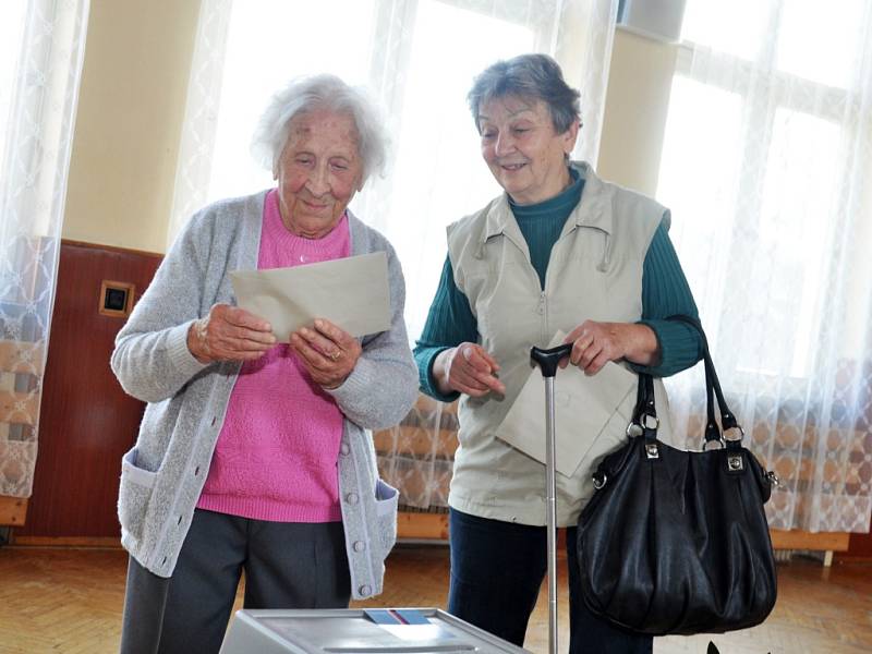 Nejstarší obyvatelka Zlínského kraje Vlastimila Češková (v růžovém), která letos na jaře oslavila 108 let, přišla v pátek 25. října 2013 do volební místnosti ve své obci jako první hned s úderem 14. hodiny. Doprovodila ji dcera Jana Kalhousová.