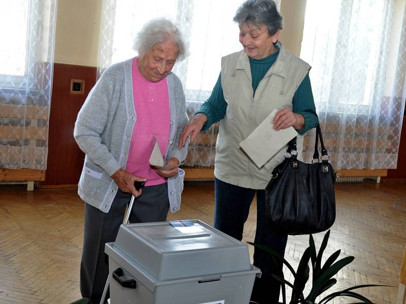 Nejstarší obyvatelka Zlínského kraje Vlastimila Češková (v růžovém), která letos na jaře oslavila 108 let, přišla v pátek 25. října 2013 do volební místnosti ve své obci jako první hned s úderem 14. hodiny. Doprovodila ji dcera Jana Kalhousová.