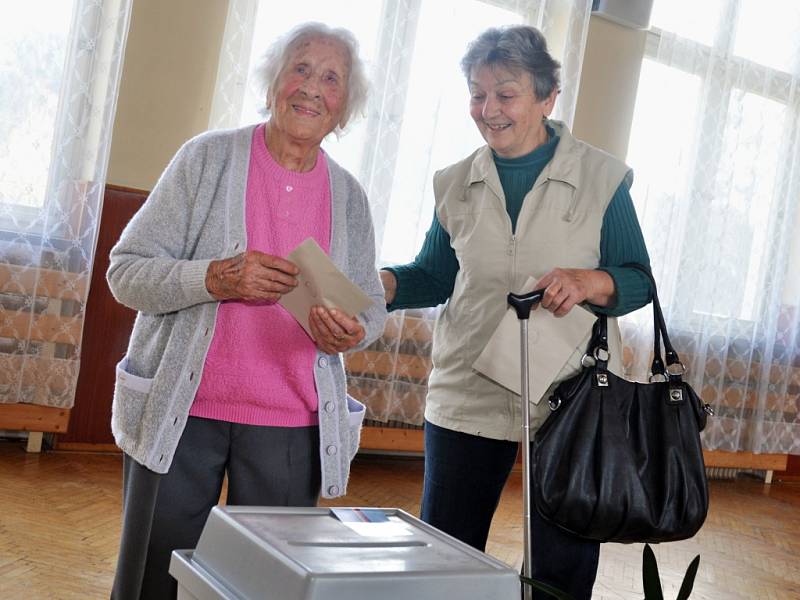 Nejstarší obyvatelka Zlínského kraje Vlastimila Češková (v růžovém), která letos na jaře oslavila 108 let, přišla v pátek 25. října 2013 do volební místnosti ve své obci jako první hned s úderem 14. hodiny. Doprovodila ji dcera Jana Kalhousová.