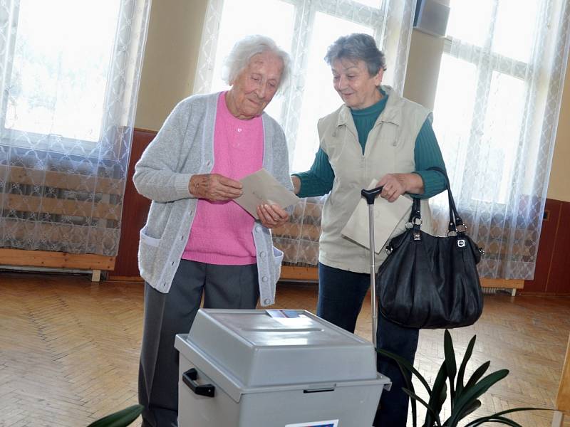 Nejstarší obyvatelka Zlínského kraje Vlastimila Češková (v růžovém), která letos na jaře oslavila 108 let, přišla v pátek 25. října 2013 do volební místnosti ve své obci jako první hned s úderem 14. hodiny. Doprovodila ji dcera Jana Kalhousová.