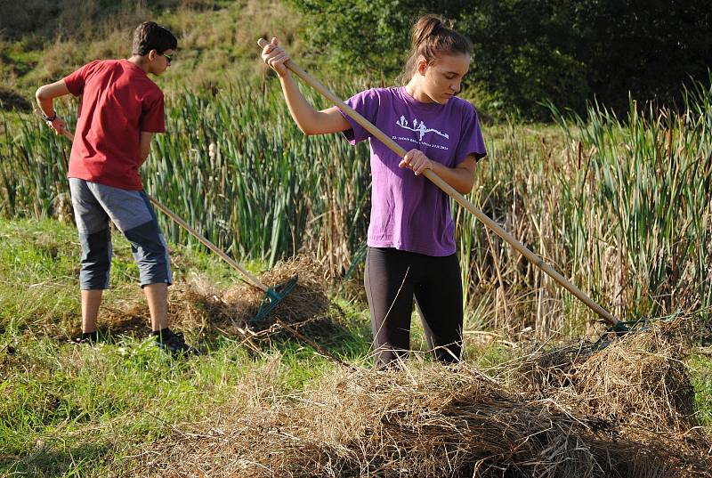 Studenti a ochránci přírody shrabují trávu.