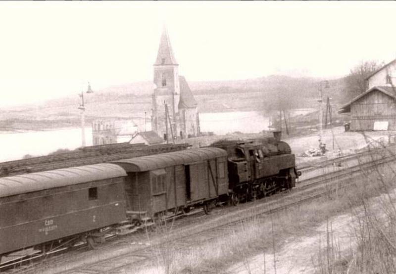 Vjezdové zhlaví stanice Dolní Kralovice. Foceno na přelomu let 1974 a 1975, v pozadí již částečně zbořený kostel sv. Jana Křtitele.
