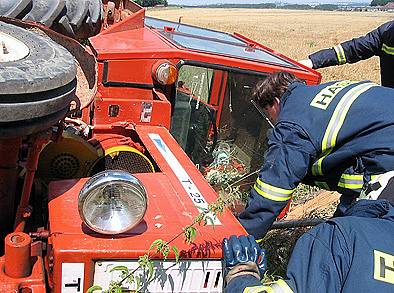 Hasiči vyprošťují převrácený traktor.