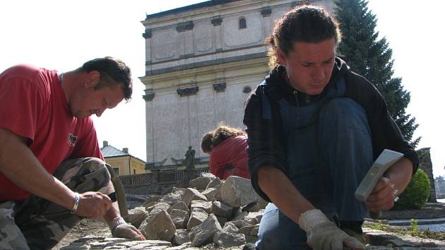 Hory větších kamenů spotřebují dlaždiči na nové chodníky. Malý kolový nakladač stále naváží další hromady kamení, které se záhy promění v trochu kostrbatou plochu. Ve středověku se jinak nedláždilo. 