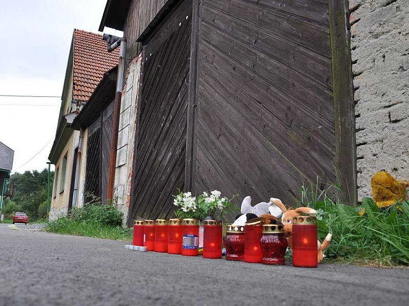 Lidé před domem zapalují svíčky. 