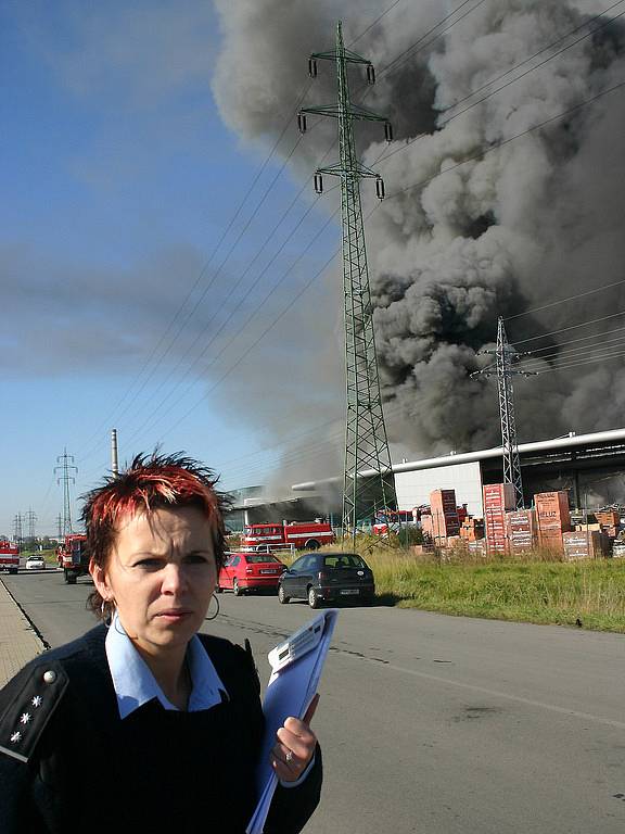 Na místo požáru přicházejí vyšetřovatelé. V pozadí je hořící továrna.