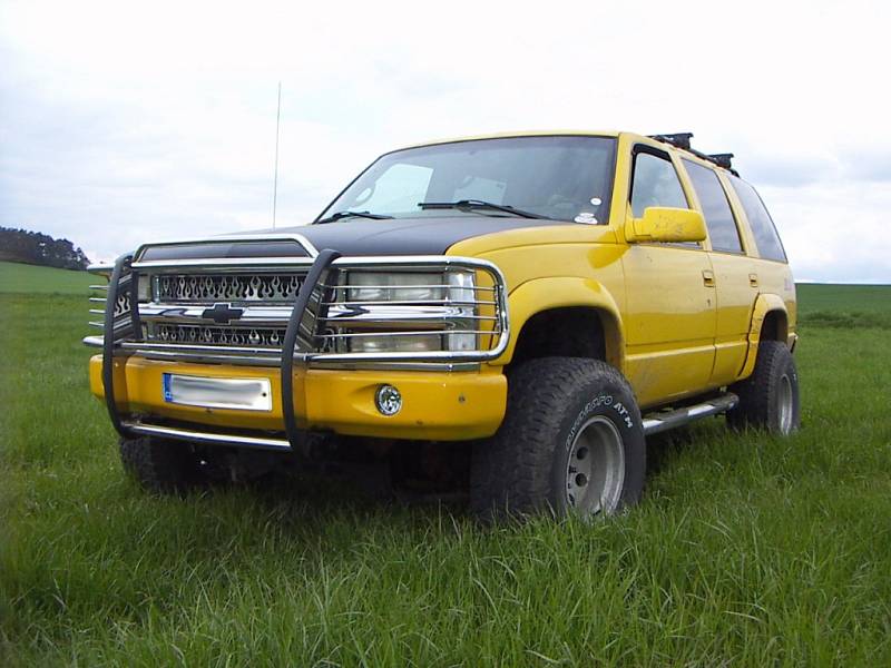 Jasně žlutý Chevrolet Tahoe Z71 ročníku 1999 s pohonem všech čtyř kol. Na první pohled zaujme leštěná mřížka chladiče se symboly plamenů.