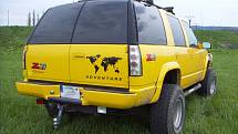 Jasně žlutý Chevrolet Tahoe Z71 ročníku 1999 s pohonem všech čtyř kol. Na první pohled zaujme leštěná mřížka chladiče se symboly plamenů.