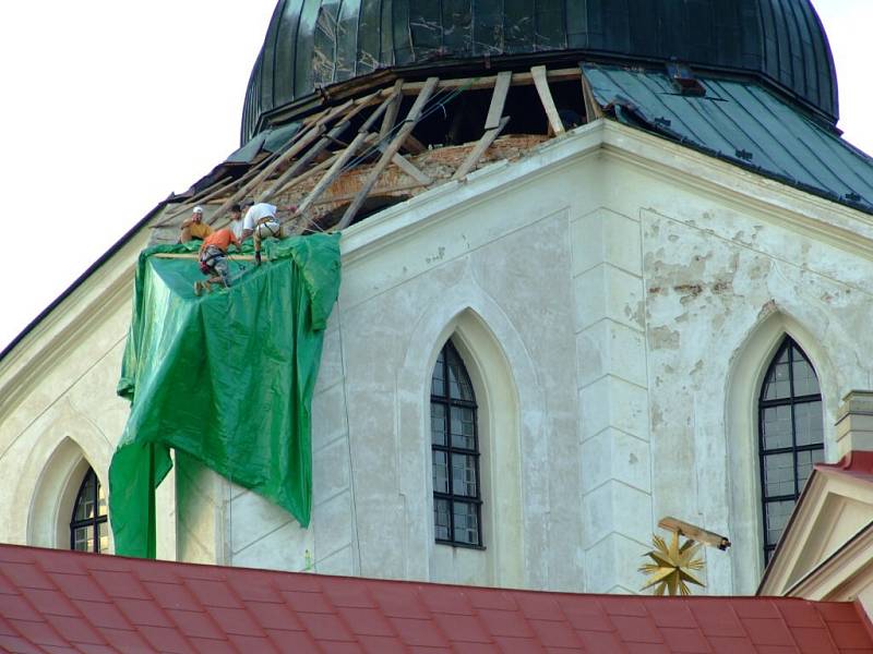 Technici instalují plachtu na poškozenou část střechy kostela.