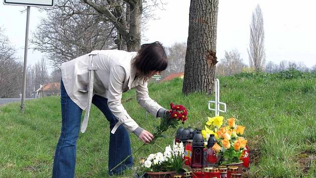 Lidé pokládají k pomníčku květiny a zapalují svíčky