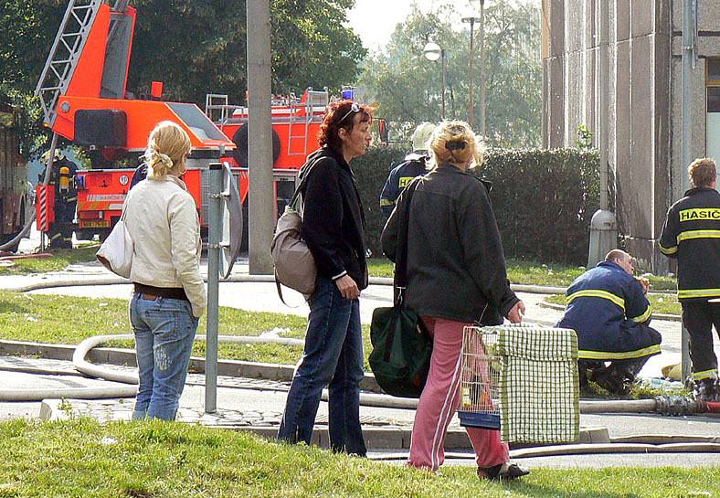 Nešťastní obyvatelé bezmocně sledují hasiče, kteří likvidují požár.