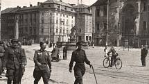 Květen 1945. Sovětští vojáci pochodují po Horním náměstí v Olomouci u poničené radnice. Orloj poškodily události války, byl přebudován v letech 1947-1955.