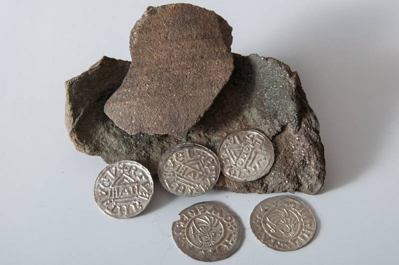Nalezené mince z 10. století, kdy vládl Boleslav II. spolu s fragmenty nádoby, ve které byly uloženy do země.