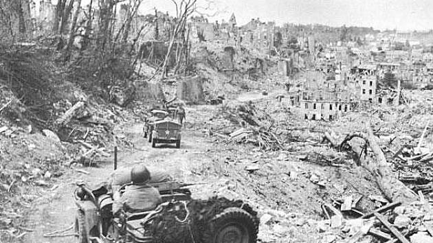 Jeep 219. dělostřeleckého praporu 35. pěší divize projíždí ruinami St. Lö