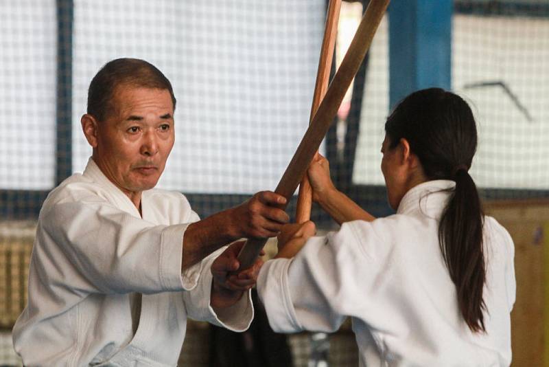 Váženým hostem, který během semináře zajišťuje zkoušky na technické stupně dan, je v Plzni japonský mistr  Tanaka Kouichi. Během naší návštěvy ukazoval studentům v hale TJ Slavia techniku úderů s dřevěným mečem boken.  