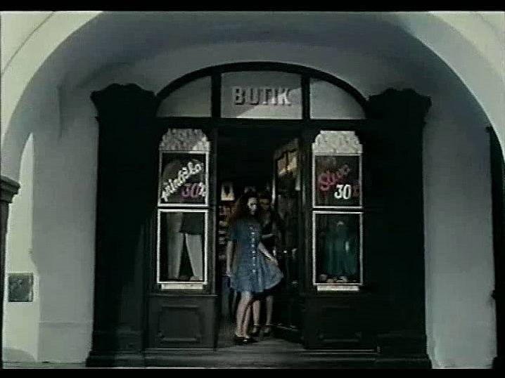 Záběr z filmu Divoké pivo. Hlavní dvojhrdinka vychází z jednoho krámku  v podloubí v Březanově ulici nedaleko náměstí.