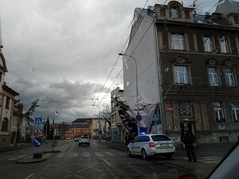 V Dukelské ulici v Českých Budějovicích u přechodu od pedagogické fakulty k Jihočeskému muzeu se utrhl billboard připevněný na stěně domu. Pomáhají ho zajistit strážníci.