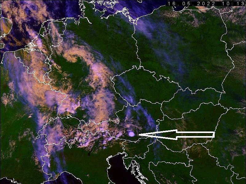 Pondělní polední radarový snímek střední Evropy. V Německu se na nás už chystá okluzní fronta (žluto-oranžový pás oblačnosti), která zvolna míří k našemu území. Na snímku je vidět i výrazná bouřka v Alpské oblasti (označena šipkou).