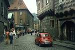 Zpěvaččin červený fiat projíždí českokrumlovskou ulicí Latrán. Auto právě míjí významný dům  čp. 15 vpravo. 