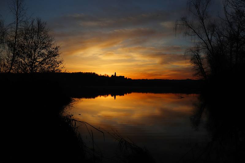 Východ slunce za zámkem Hluboká nad Vltavou přes rybník Munický, který je plný ptactva a romantických zákoutí na hrázi.