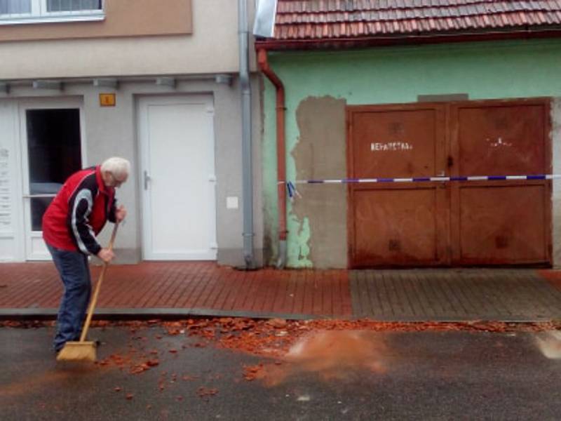 Muž před domem uklízel rozbité tašky ze střechy v Českých Budějovicích v Baarově ulici.