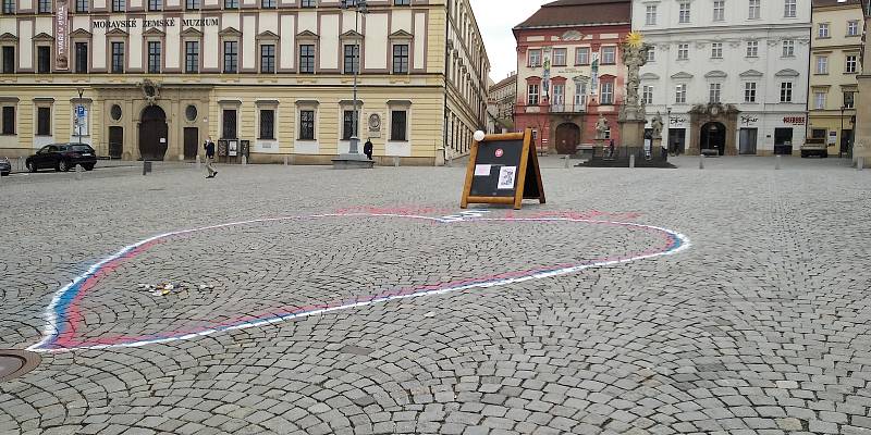 Lidé vkládají pomalované kamínky do srdce na Zelném trhu.