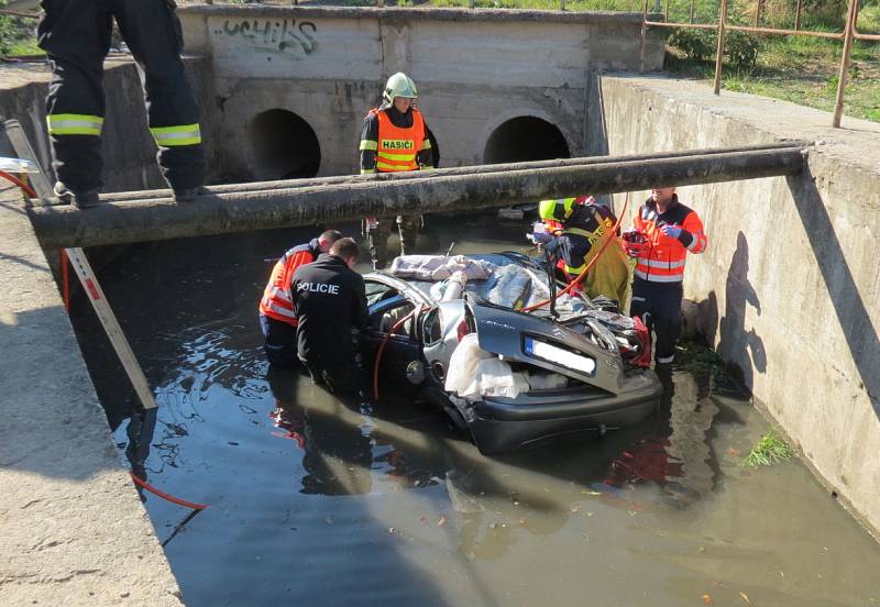 Auto převrácené na střechu potopené střechou do bahna. Řidič v něm zůstal připoutaný k sedadlu. A zraněný.