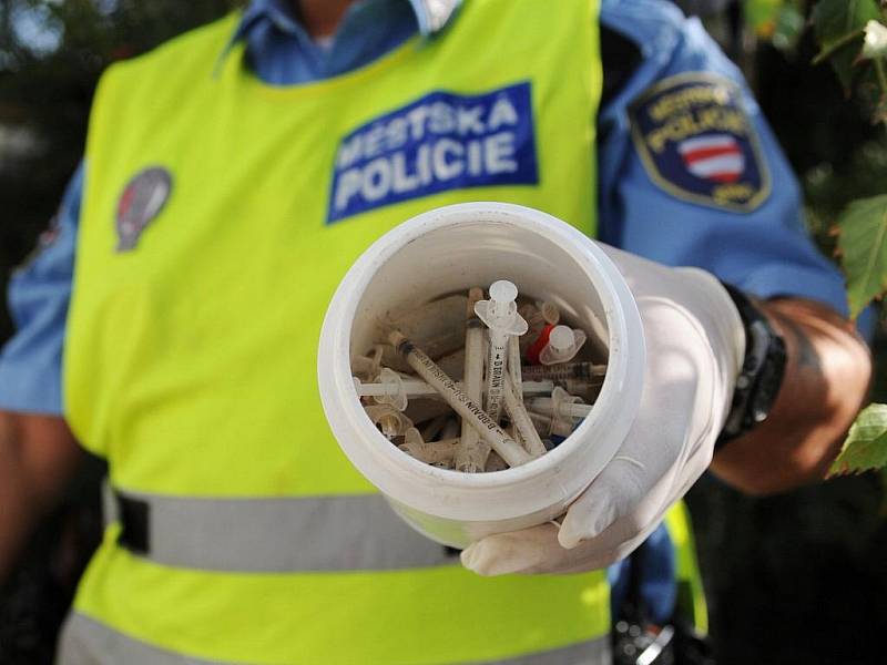 Strážníci sbírají injekční stříkačky po narkomanech.