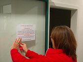 Zaměstnankyně centrálního příjmu sokolovské nemocnice, vyvěšuje oznámení o zákazu návštěv.