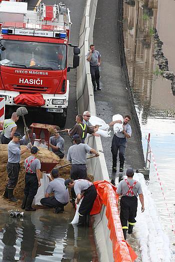 Voda zatopila Přístavní ulici v Ústí nad Labem. Na místě zasahují profesionální i dobrovolní hasiči, kteří pytlují vaky, kterými se snaží utěsnit komunikaci. Vodu z ní poté odčerpají.