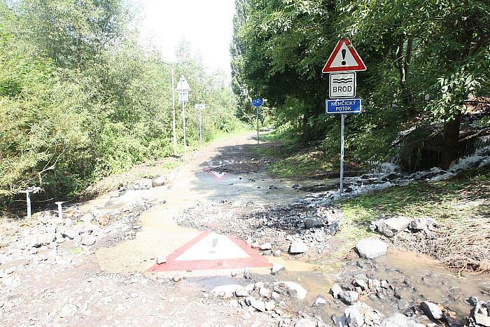 Nánosy bahna, kamení a proud vytkající vody na silnici v Sebuzíně. I přes dopravní značku zakazující vjezd tudy stále projíždějí nejen řidiči aut, ale i cyklisté.