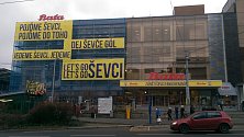 BERANI, DO TOHO! Budova prodejny Baťa ve Zlíně v Dlouhé ulici se oblékla do modré plachty, na které žlutě září například nápis Dej, ševče, gól!