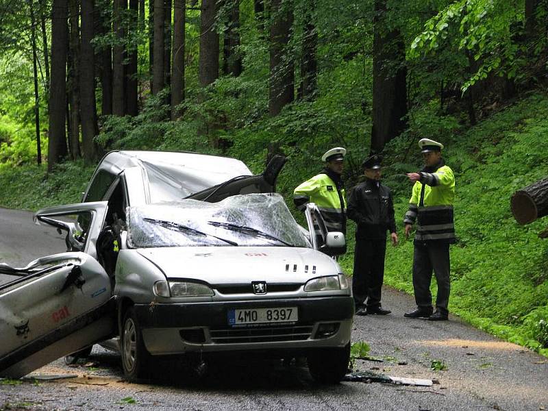 Zdemolované auto, na které spadl strom. V bílém pytli je zabalena žena, která ve vozidle zemřela