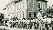 SPARTAKIÁDA. Cvičenci na snímku z roku 1970 se řadí ke slavnostnímu průvodu obcí ke kulturnímu domu, kde proběhne místní spartakiádní cvičení. Na fotografii jsou žáci základní školy s učitelem Karlem Štefkem s budovou základní školy v pozadí.