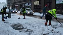 Pracovníci technických služeb odhrnují sníh na přechodu pro chodce u velké pasáže.