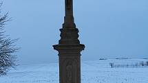 Hostějov se sněhovou pokrývkou. Kříž u příjezdu do vesnice.