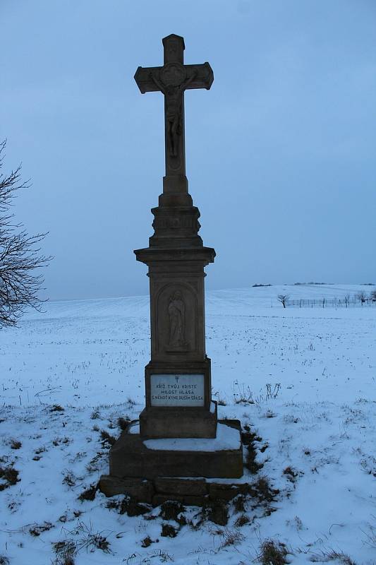 Hostějov se sněhovou pokrývkou. Kříž u příjezdu do vesnice.