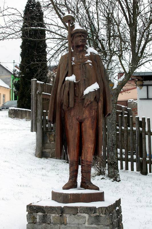 Dřevěná socha fašankového gazdy – fašančára v životní velikosti, která se podobá místní dvojici folkloristů Stanislavu Popelkovi a Františku Jankových.