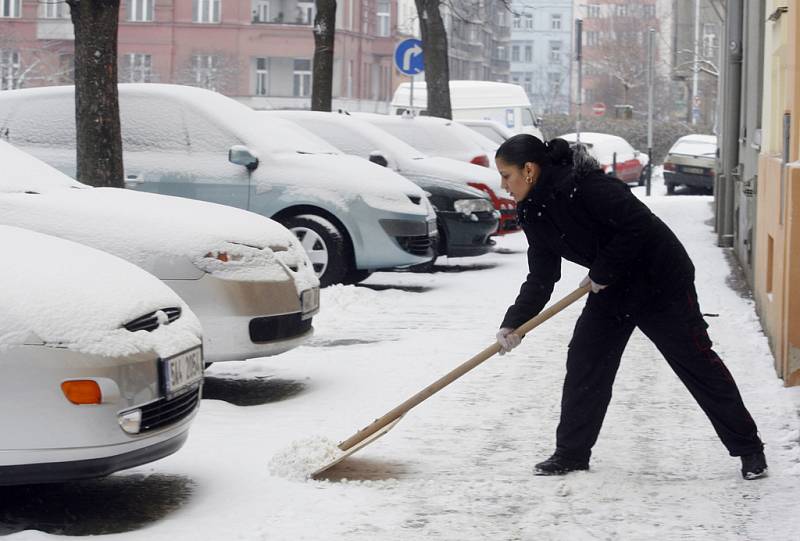 Mladá žena odklízela čerstvě napadaný sníh z chodníku v Blodkově ulici v Praze na Žižkově. 