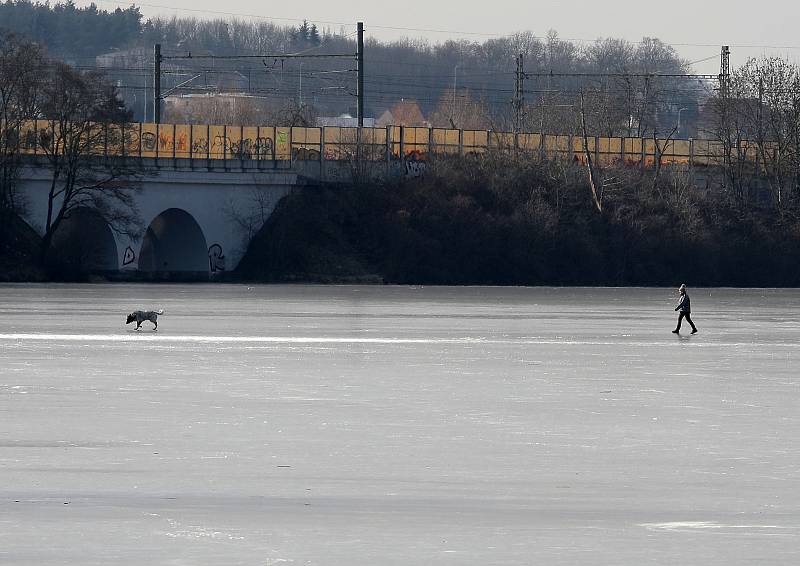 Ledová Praha - zamrzlý Kyjský rybník. Lidé si přes něj zkracují cestu na vlak, maminky bruslí s kočárkem a hraje se tu hokej.