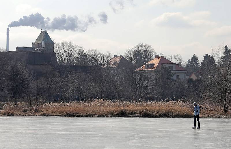 Ledová Praha - zamrzlý Kyjský rybník. Lidé si přes něj zkracují cestu na vlak, maminky bruslí s kočárkem a hraje se tu hokej.