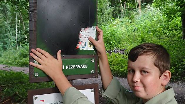 Mladý pomocník stráže přírody vyměňuje smaltovanou ceduli s posprejovaným malým státním znakem.